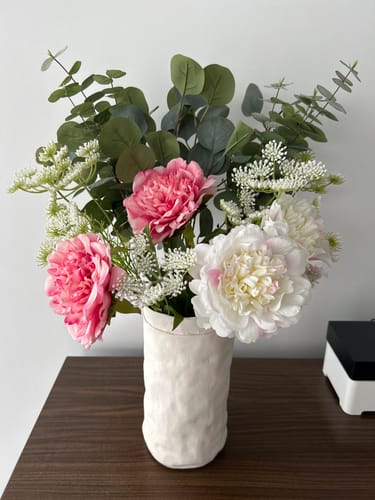 Een klant toont Boeket Maïa, een vol boeket met roze en witte pioenrozen in een witte vaas.