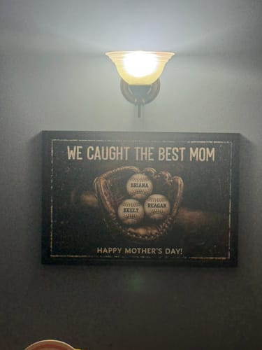 Customer's framed 'We Caught The Best Mom' personalized poster hanging on a dark wall under a light fixture.