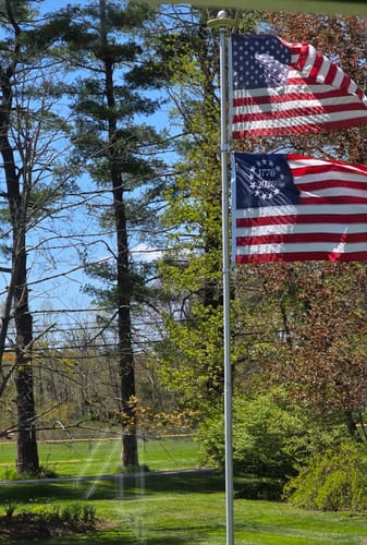 Customer's Betsy Ross flag flying below a US flag on a flagpole in a yard.