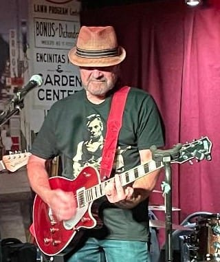 Customer on stage wearing the dark Lincoln Guitar T-Shirt while playing a red guitar.