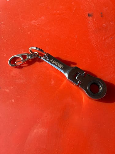 Reviewer's shiny 10mm Wrench Keychain from 80Eighty laid out on a bright red surface.