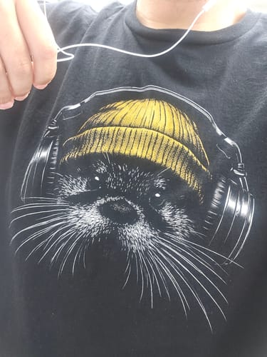 Close-up of a customer wearing the black Otter Tune t-shirt, featuring its graphic of an otter in a yellow beanie and headphones.