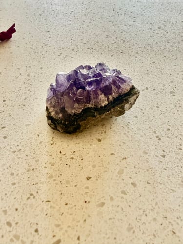 Customer's amethyst crystal cluster with deep purple points shown on a white countertop.