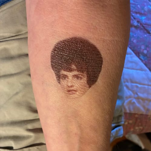Customer's forearm with a Custom Photo Face Temporary Tattoo of a face with a large, dark hairstyle.