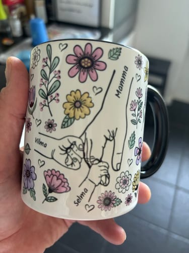 Kund som håller i sin Kärleksmugg med ett personligt tryck av händer, namn och fina blommor.