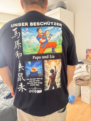 Rückansicht eines Kunden, der das personalisierte schwarze T-Shirt 'Unser Beschützer' mit einem bunten Anime-Aufdruck trägt.
