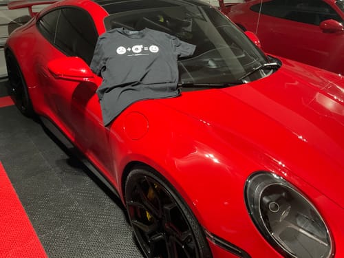 Customer's black HappyTurbo Shirt displayed on the hood of a shiny red sports car in a garage.