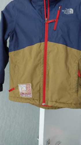 Customer's Morzine Woven Patch sewn onto the bottom of a child's blue and tan jacket.