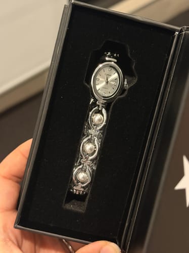 Customer showing the silver-toned PERLE DE MAINS watch with its pearl-adorned band inside its black box.