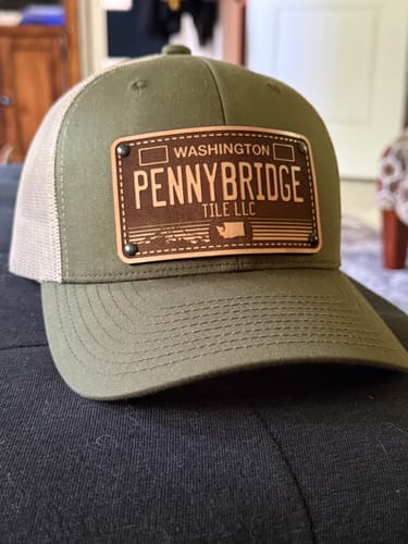 Customer's green trucker hat with the custom Washington Engraved License Plate patch reading 'Pennybridge Tile LLC'.