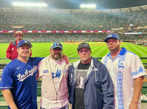 Customer wearing the white LA All Day Guayabera with blue details, posing with a group at a baseball stadium.