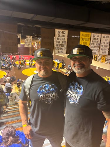 Two customers wearing their matching black California 60's Plate Hats at an indoor wrestling event.