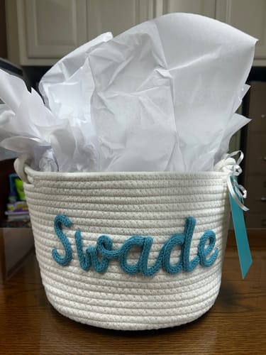 Customer's personalized white rope basket with the name 'Swade' in blue yarn, filled with tissue paper.