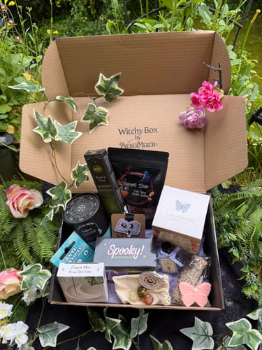 Kunde zeigt die geöffnete Witchy Box Mai, gefüllt mit verschiedenen mystischen Produkten, in einer grünen Umgebung.