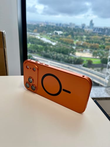 Customer's orange MagCase Metal showing the back with the MagSafe ring and camera protection on a table.