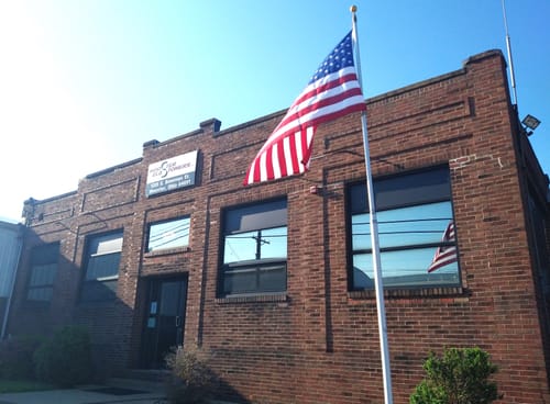 Customer's durable American flag waving on a flagpole in front of a brick building.