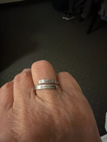 Customer's hand wearing the silver Just Breathe Ring engraved with 'Just breathe' and a small heart.