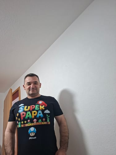 Ein Kunde trägt sein personalisiertes schwarzes 'Super Papa'-T-Shirt.