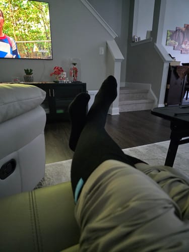 Reviewer relaxing with their feet up while wearing black Eucalyptus Lyocell Compression Socks in a living room.