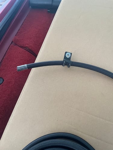 Customer's 1/2" Line Clamp with a black rubber cushion securing a black braided hose against a cardboard background.