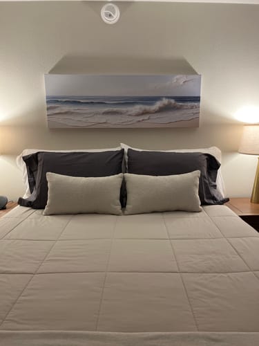 Customer's Ocean Wave Seascape Wall Art hanging above a neatly made bed in a calm bedroom.