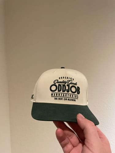 Customer holding a Big Structured A-Frame Hat, showing its off-white crown, dark green bill, and a black logo.