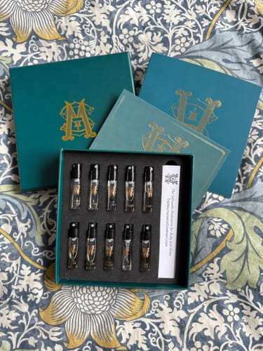 Customer's open Discovery Set showing ten small fragrance vials arranged in a teal box on a floral surface.