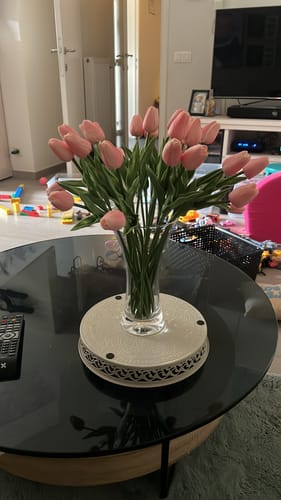 Recensent toont het boeket roze tulpen in een glazen vaas op een salontafel.