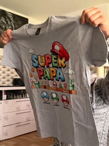 Ein Kunde hält das graue, personalisierte Super Papa T-Shirt hoch.