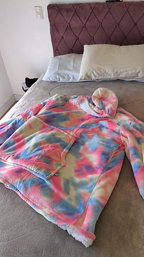 Avaliador mostrando o Sleepo Tie Dye com estampa tie-dye colorida sobre uma cama.