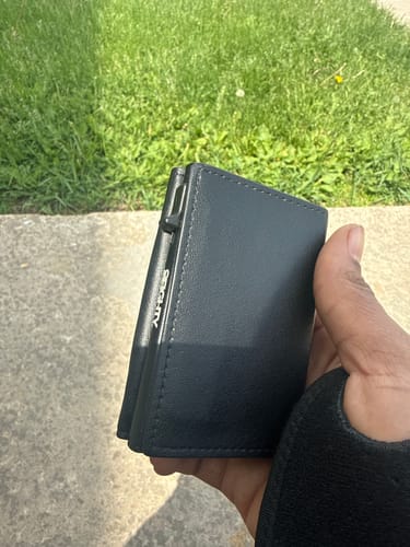 Customer holding the black Onyx Wallet in their hand outdoors, showing its compact size and side profile.
