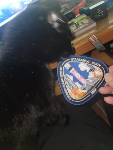 A reviewer holds the Starship Flight 12 Collectors Patch while a black cat looks at it.