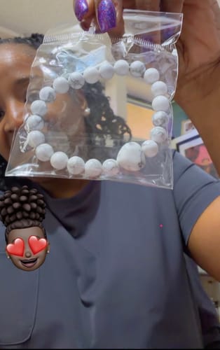 Customer holding a white crystal bead bracelet with a heart accent in its original clear packaging.