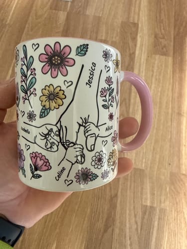 En kund håller upp sin Kärleksmugg med ett personligt tryck av namn, händer och färgglada blommor.