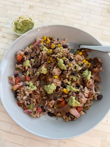 Reviewer's prepared Steak Burrito Bowl in a white bowl, with chimichurri sauce on top and in a side container.