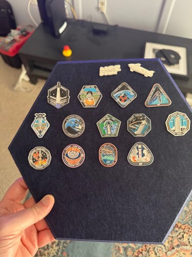 Reviewer showing their Starship Flight 12 Collectors Pin as part of a collection on a blue hexagonal board.