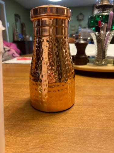 Customer's shiny Diamond-Cut Copper Water Bottle sitting on a wooden table.