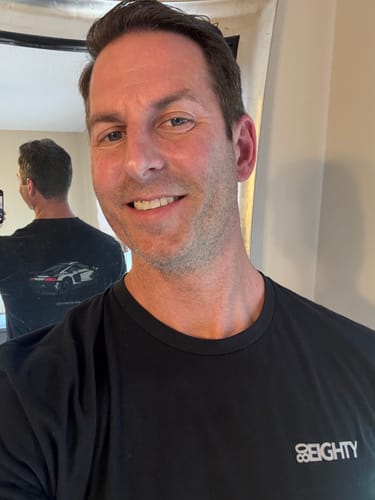 Reviewer in a mirror selfie wearing the black DCG89 Shirt, showing the front logo and the back car graphic in the reflection.