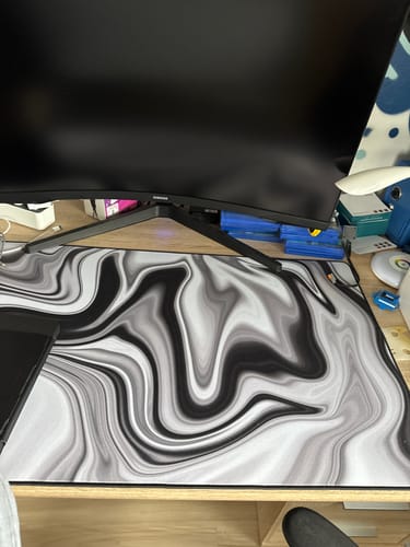 Rezensent zeigt das RZ Mousepad Liquid Black & White auf einem Schreibtisch unter einem Monitor.