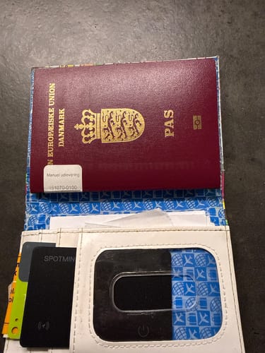 Customer's black SPOTMINDERS Tracking Card placed inside a passport cover next to a Danish passport.