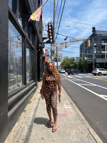 Customer walking on a sidewalk, providing a full front view of the leopard print Naked Print Halter Capri Jumpsuit.