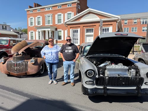 Customer wearing the black Love My Wife Shirt while standing between two classic cars outdoors.