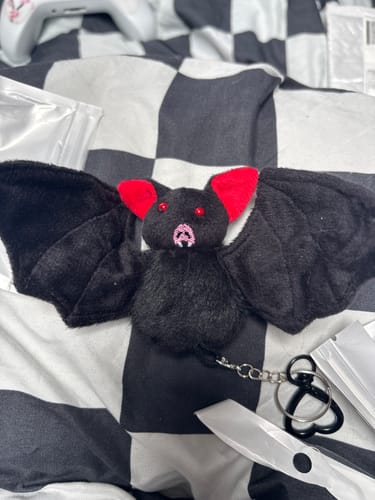 Customer's plush black bat keychain with wings spread open, showing red inner ears and red eyes on a checkered surface.