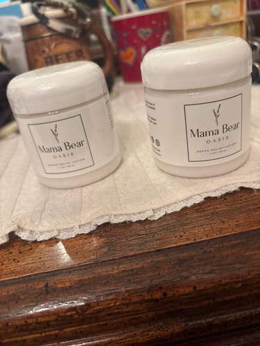 Reviewer's two jars of Mama Bear Nerve Relief Lotion sitting on a wooden dresser.