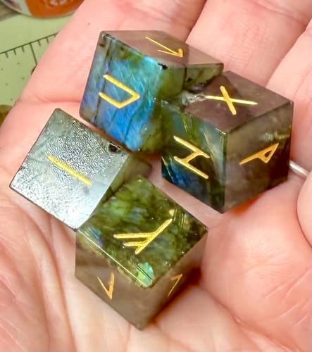 Customer holding a set of iridescent labradorite rune dice in their palm, showing the gold engravings.