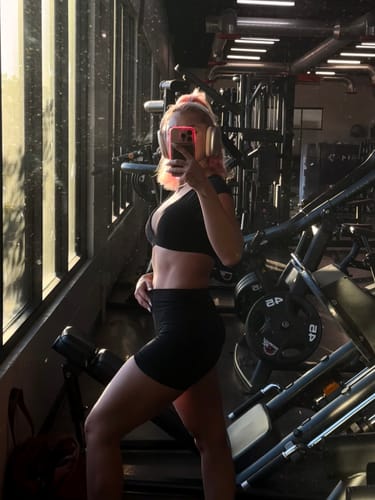 Customer takes a mirror selfie at the gym, wearing the black Amore Cap Sleeve Bra.