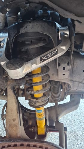 Customer's silver Forged Aluminum Upper Control Arm installed above a yellow strut on a truck's wheel assembly.