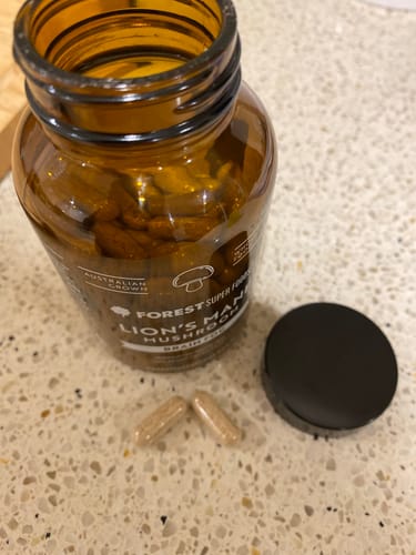 Customer's open bottle of Mini Australian Grown Lions Mane Capsules with two capsules out on a counter.