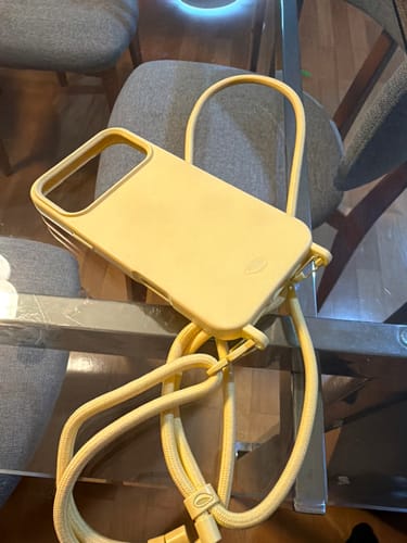 Case Nora do cliente na cor amarelo manteiga com a alça, sobre uma mesa de vidro.