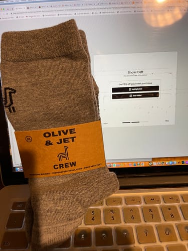 Customer's new pair of brown Crew Socks in their packaging, held over a laptop.